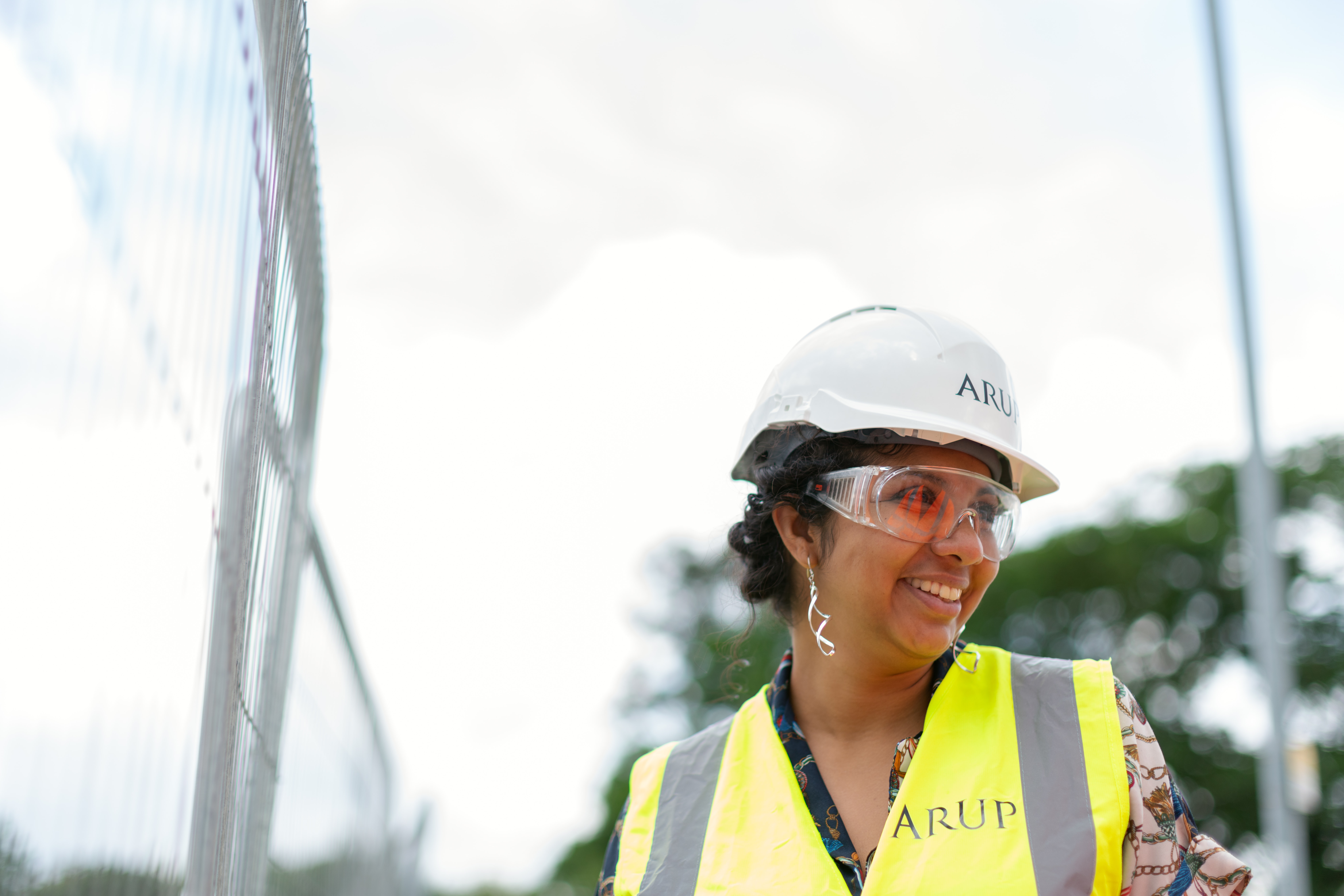 Woman with white hard hat and yellow safety vest on standing in front of scaffolding
