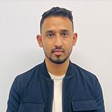 Mandip posing in front of a white wall with a navy button up shirt on